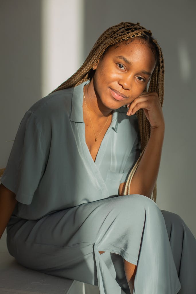 Smiling woman with long braids in casual attire, seated indoors with natural light.