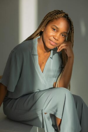 Smiling woman with long braids in casual attire, seated indoors with natural light.